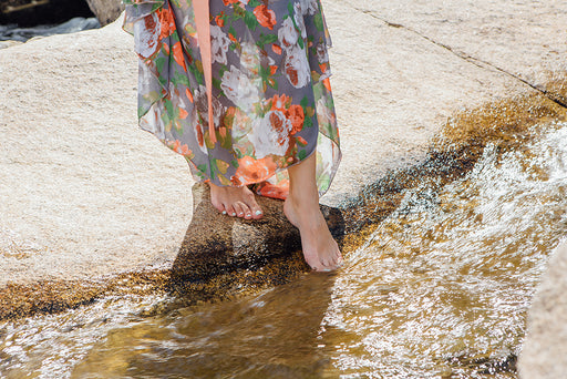 a woman in a floral dress dipping her toes in running water