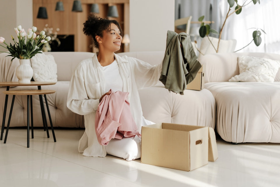 a woman sorting through her clothing and putting her choices for donation into a cardboard box