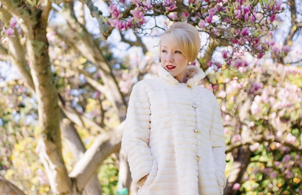 Phoebe standing under tree blossom wearing a 1960’s coat