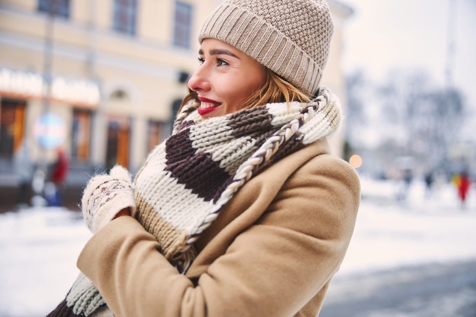 a woman looking cosy in a camel coat with woolen gloves, scarf and hat