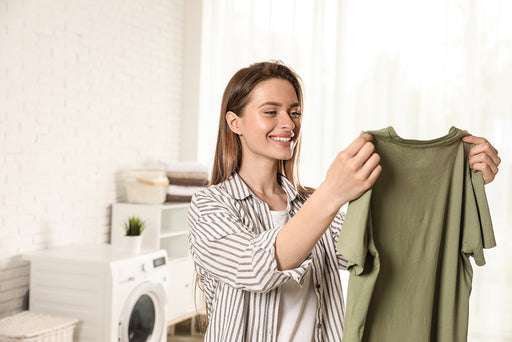 a smiling woman in the laundry room holding up a clean green tee