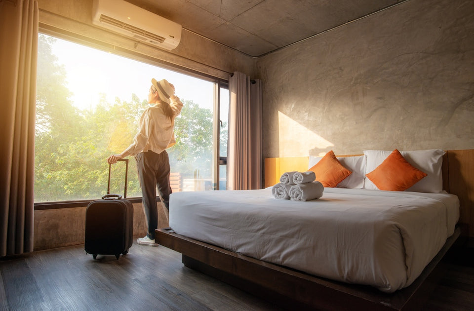 a female traveller, standing by her suitcase in her hotel room looking out the window