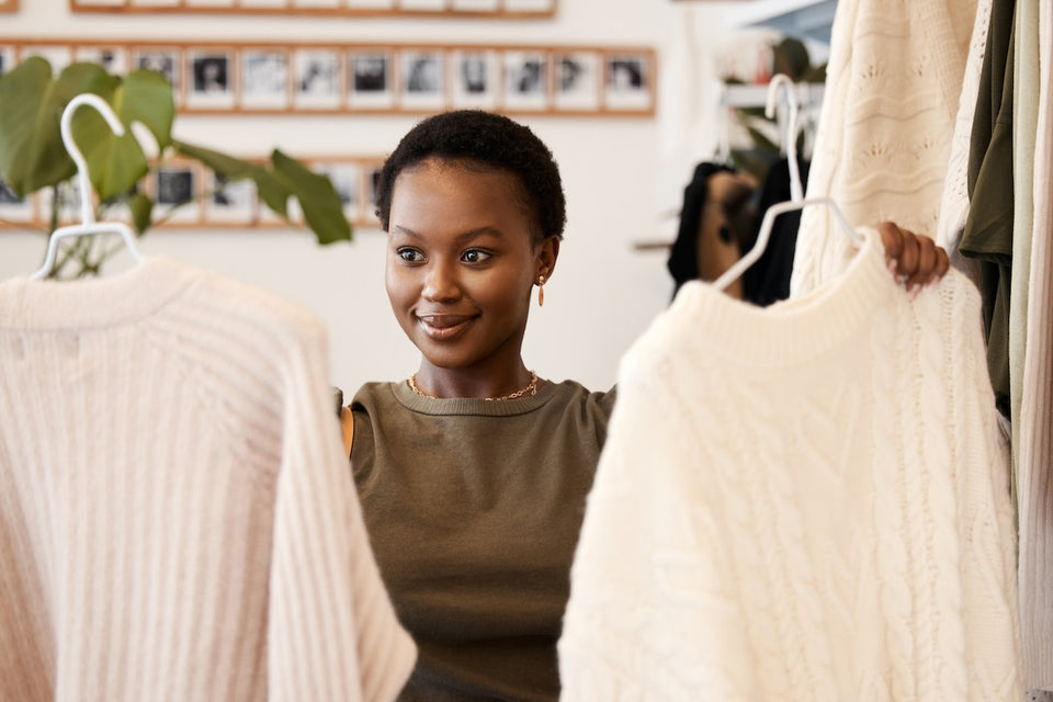 a woman in a clothing shop deciding which cream woollen sweater to buy