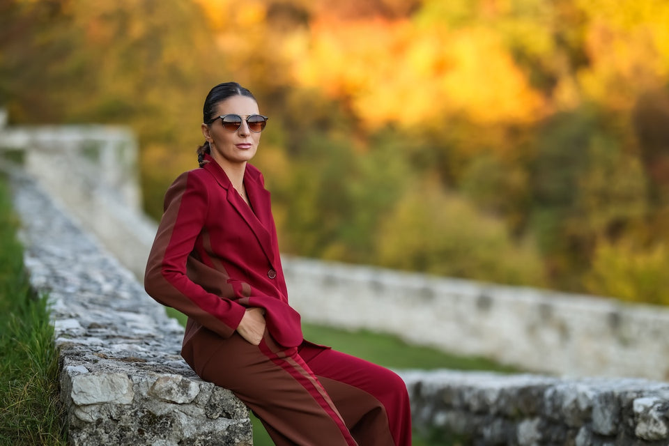 a woman wearing a tailored burgundy trouser suit and sunglasses
