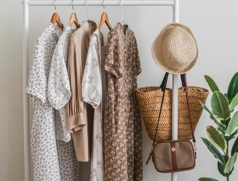 some patterned dresses neatly placed on a clothes rail with a straw hat and purse