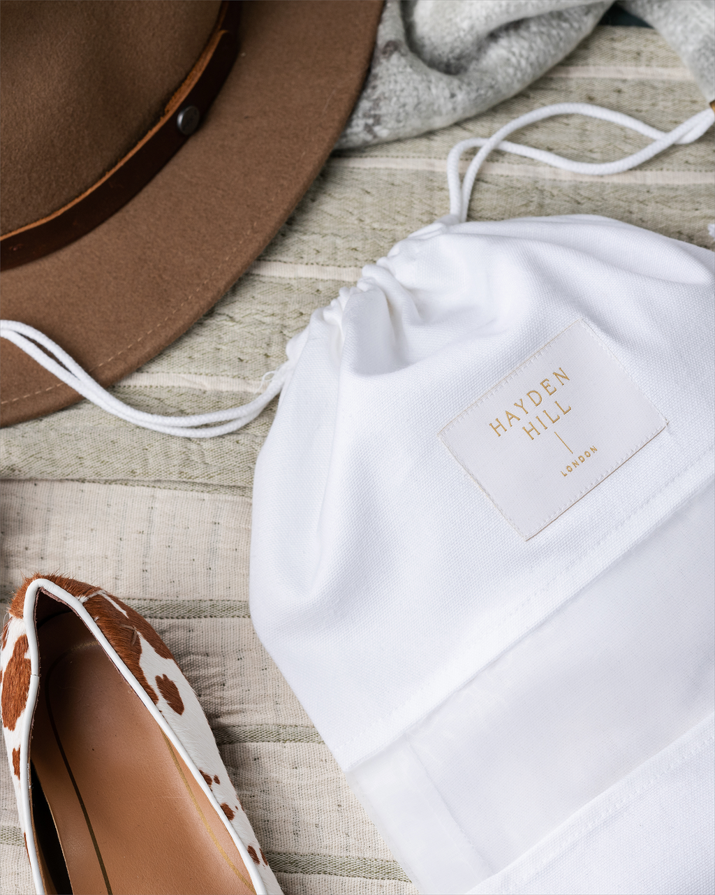 a dust bag next to a pair of pony skin loafers and a felt hat
