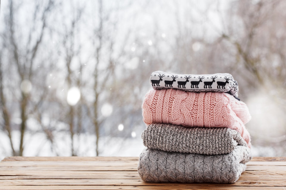 a pile of woolen sweaters sitting on a wooden table with a snowy winter background