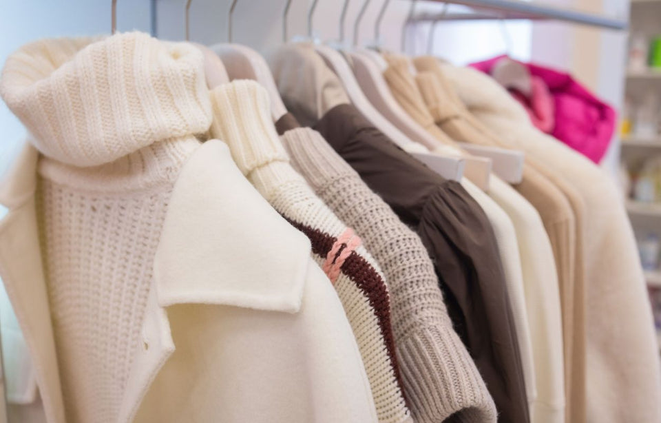 row of beautiful cream and beige natural knits hanging in a store