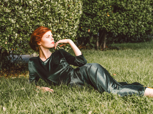 a glamorous woman wearing a green velvet dress lying in green grass