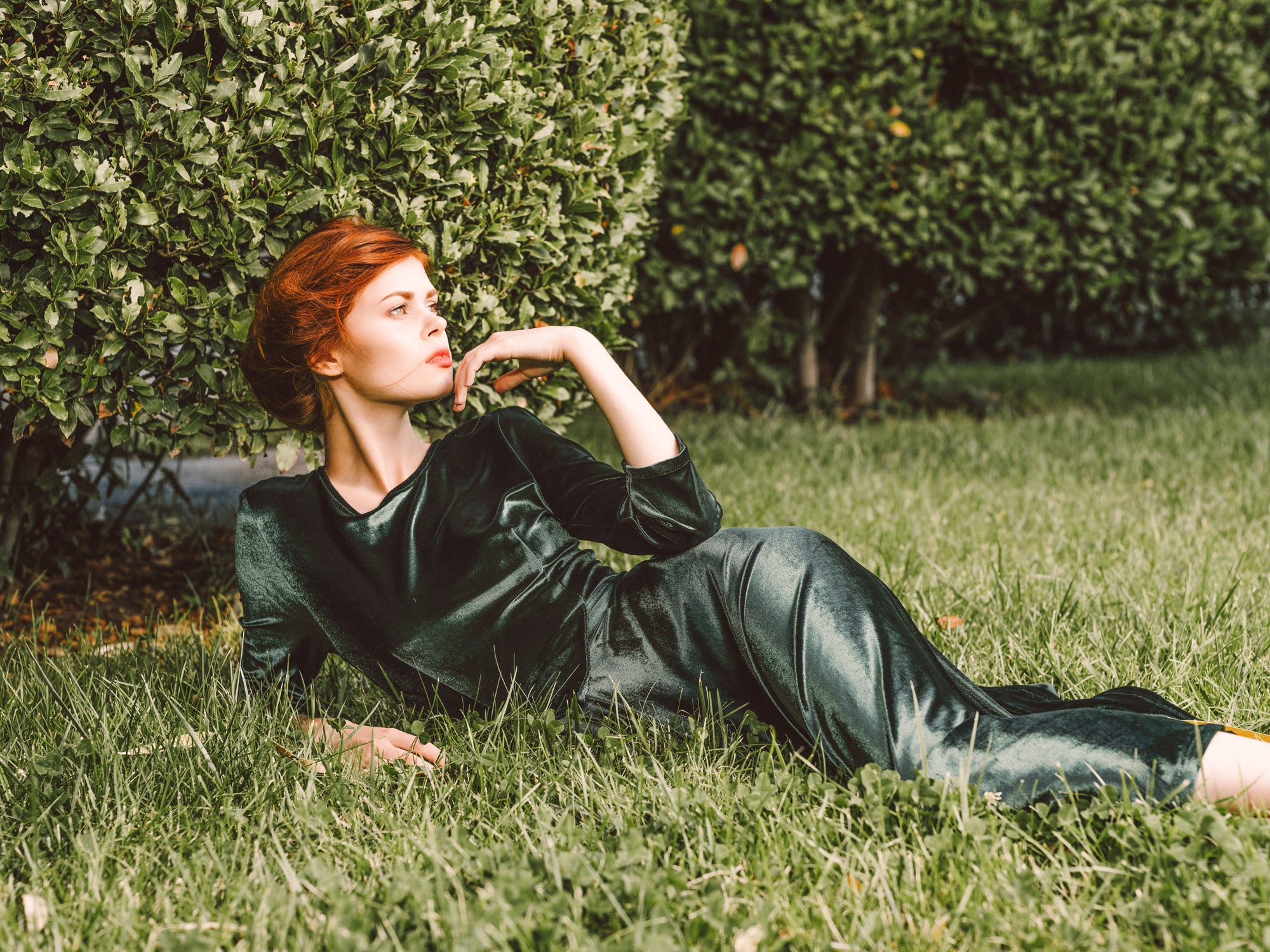 a glamorous woman wearing a green velvet dress lying in green grass