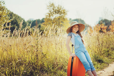 a young girl in a sunny field, leaning on a suitcase