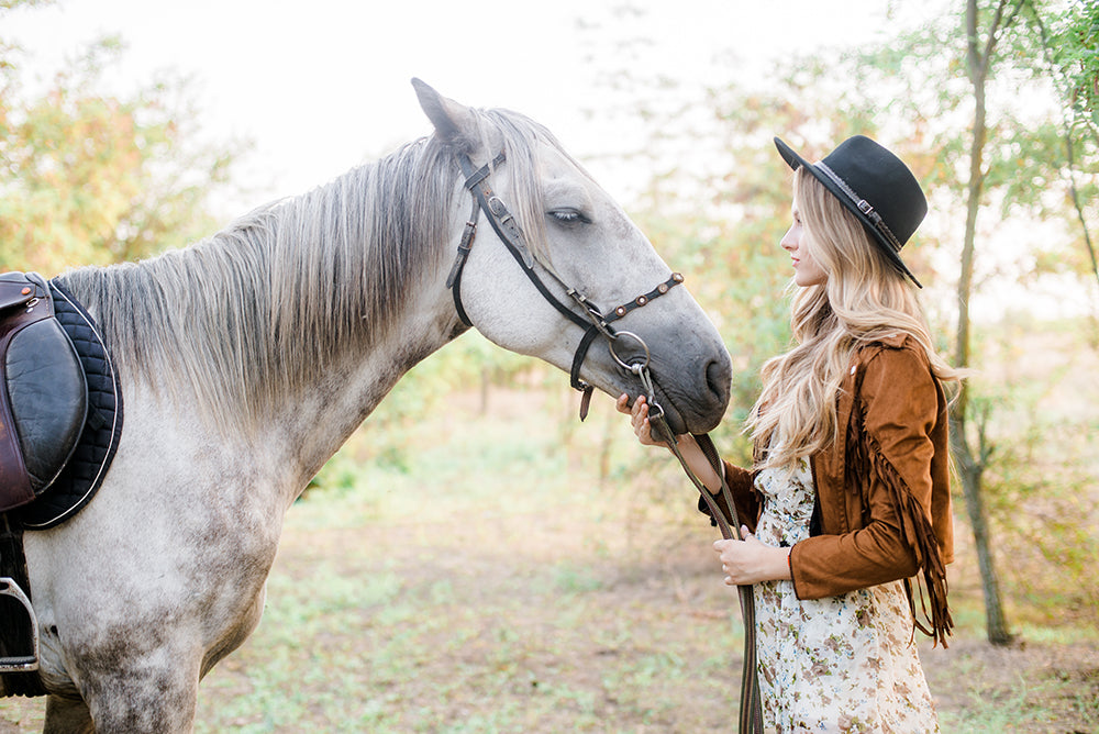 a woman wearing a leather fringed jacket holding her horses reins