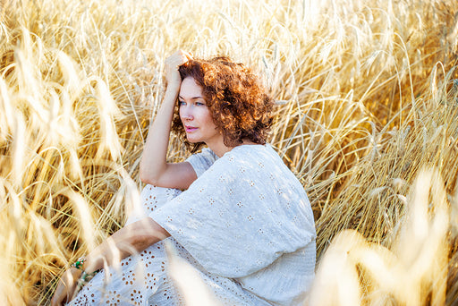 a beautiful woman in a white cotton dress sitting in a wheat field