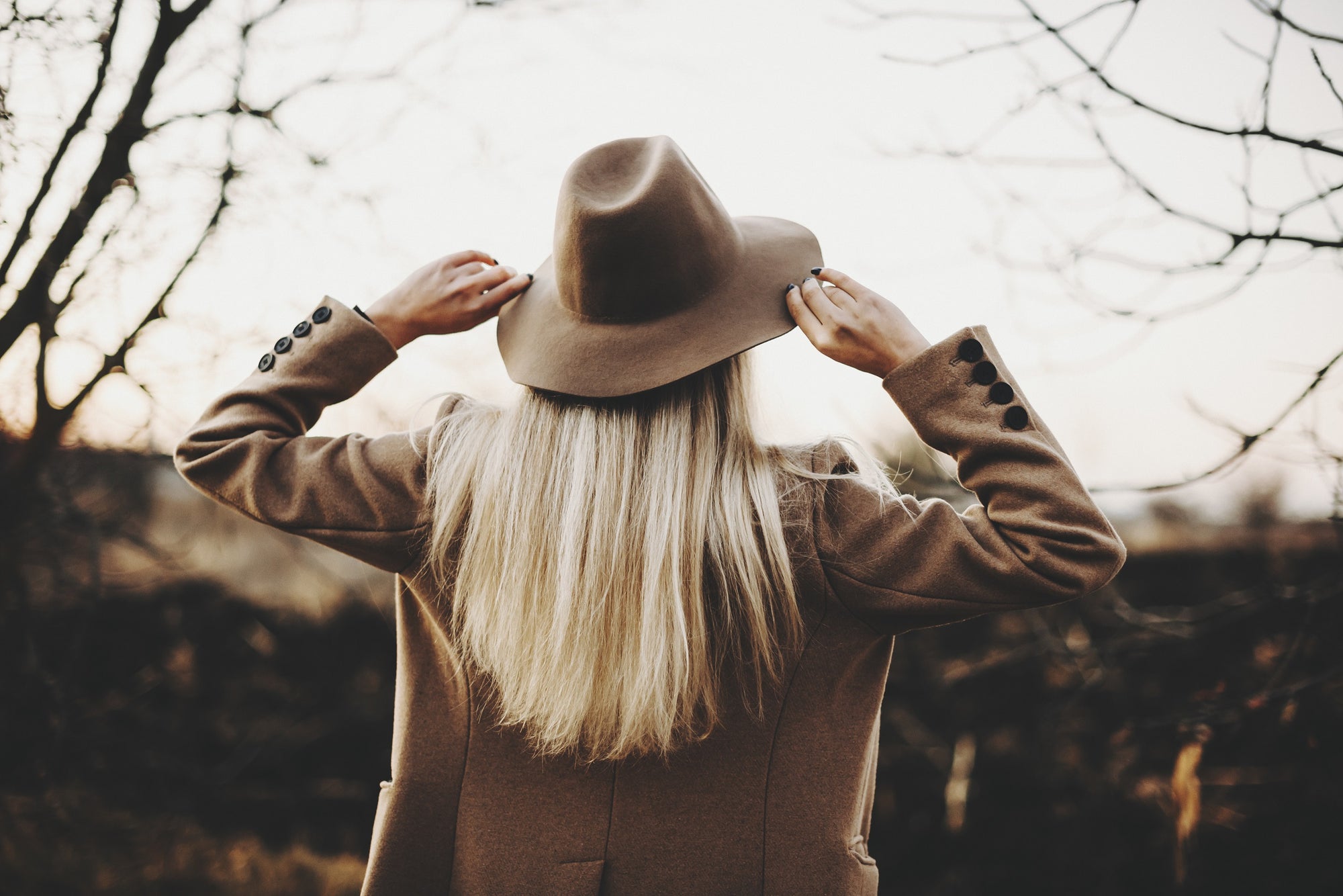 a woman with her back to the camera wearing a felt hat and a camel wool coat