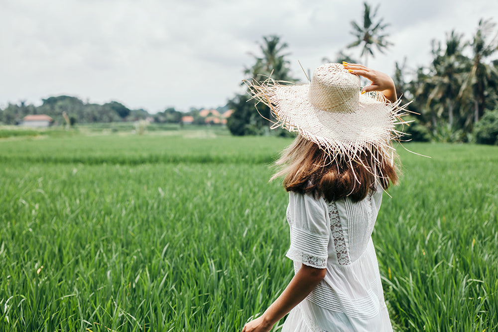 a woman wearing a vintage white dress and straw hat looking over a field