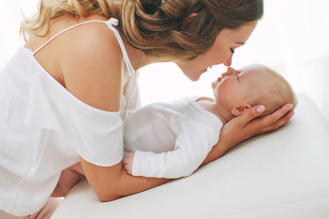 a baby, wearing a white soft top made from modal fabric, being embraced by his mother