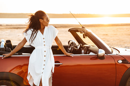 a stylish woman in a white button down dress leaning against her car