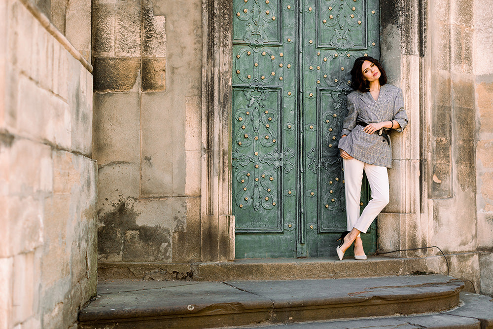 a woman wearing smart white ankle length trousers leaning against a green door