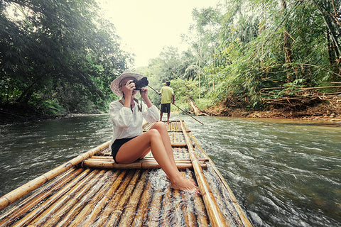 a photographer sitting on a bamboo raft taking photos whilst traveling down a river