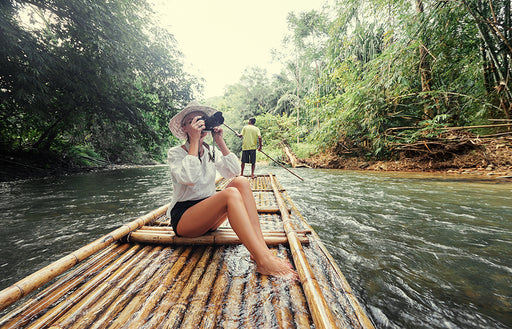 a photographer sitting on a bamboo raft taking photos whilst traveling down a river