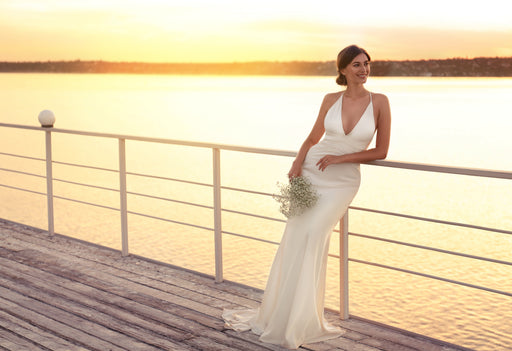 beautiful bride in a cream satin dress, with the sun setting behind her