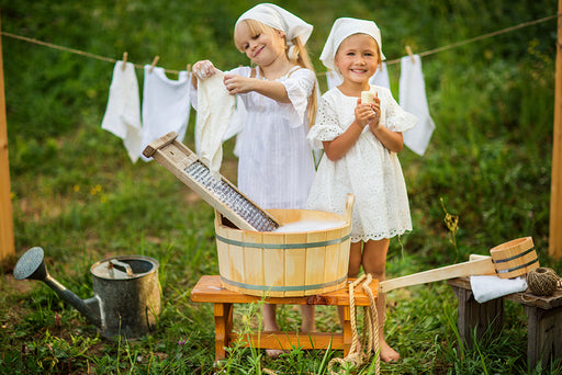 two children doing having fun doing laundry with an old washboard and wooden tub
