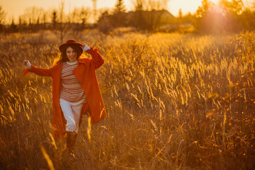 a woman in an orange coat and patterned sweater running through a golden field of grasses