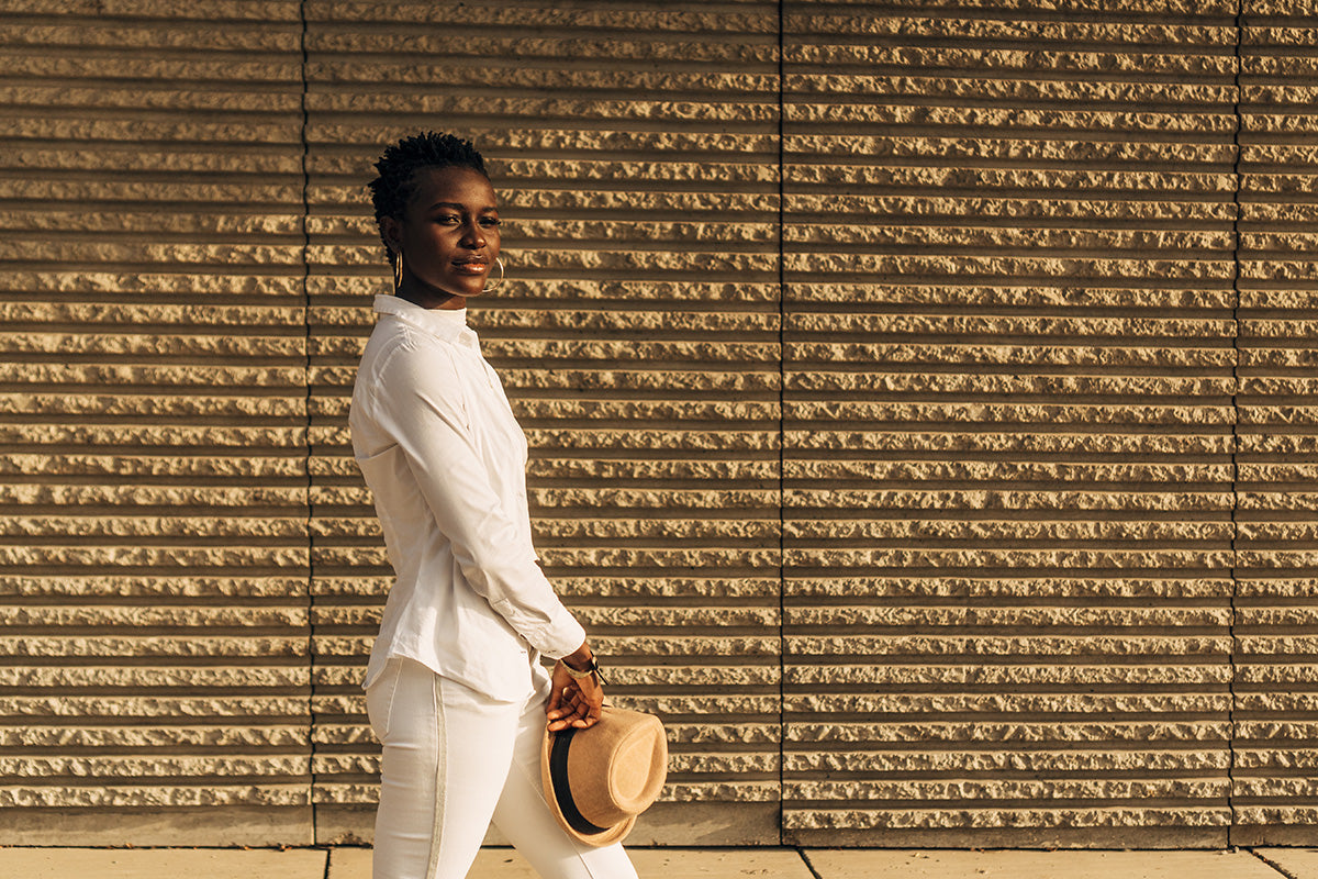 a chic woman wearing a cream shirt and cream pants, carrying a straw panama hat