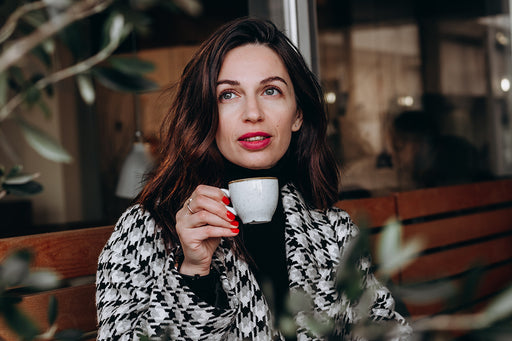 an elegant woman wearing a houndstooth coat and drinking her coffee