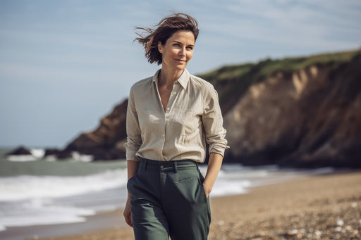 a woman walking on the beach in a linen shirt and dark green pants