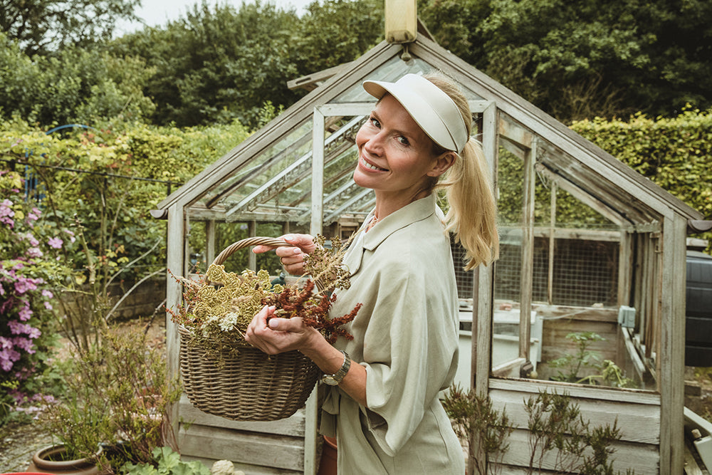 a woman carrying a basket of dried flowers in front of a greenhouse