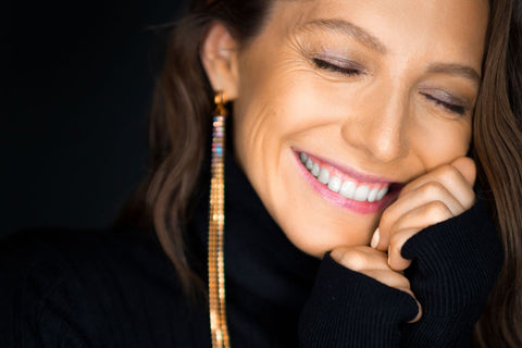 a close up of a smiling woman in her forties wearing long dangly earrings