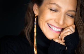a close up of a smiling woman in her forties wearing long dangly earrings