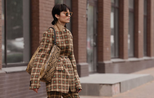a very fashionable woman in sunglasses wearing a checked brown suit and snakeskin handbag