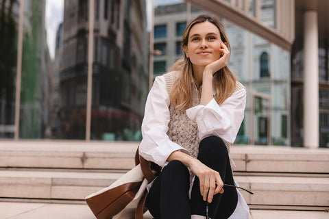 Meta: a woman sitting on steps dressed in a casual white shirt, chunky knit vest and leggings