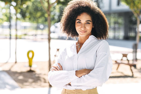a woman standing outside wearing a white shirt and sand colored pants