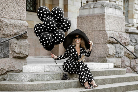 a woman wearing a black and white polka dot jumpsuit and large brim hat, holding black and white polka dot balloons