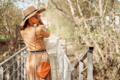 a woman wearing a hat and dressed in caramel-colored vest and pleated skirt