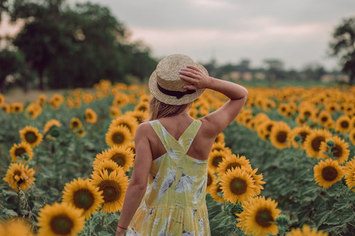 a woman with her back to the camera in a sundress standing in a field of sunflowers