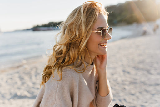 a woman in sunglasses and a cashmere sweater sitting on the beach