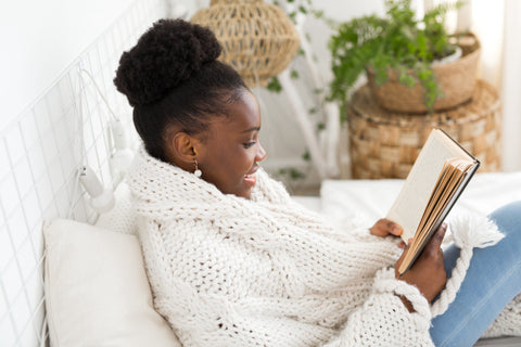 a woman reading and relaxing, wrapped in a white wool blanket