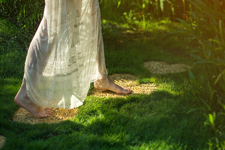 a woman in a lace skirt and bare feet walking on pebble heart-shaped stones