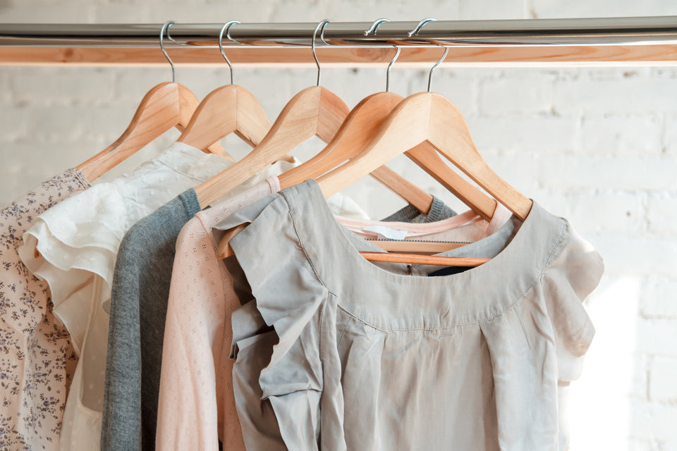 a variety of clothing hanging on wooden hangers on a rail