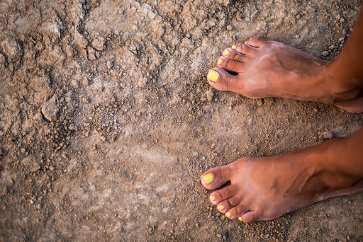 bare feet with manicured yellow nail varnish standing on dry earth