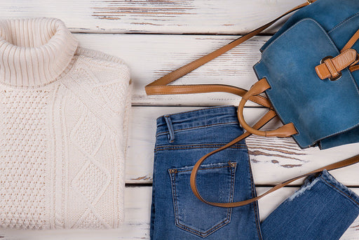 a neatly arranged outfit including a cream sweater, pair of sneakers, jeans and a duffel bag