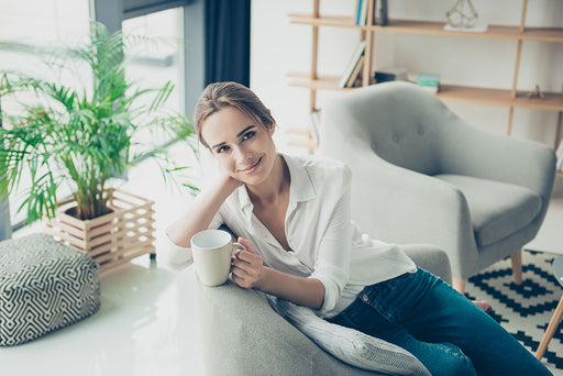 a woman wearing jeans and a white shirt relaxing at home with a hot drink