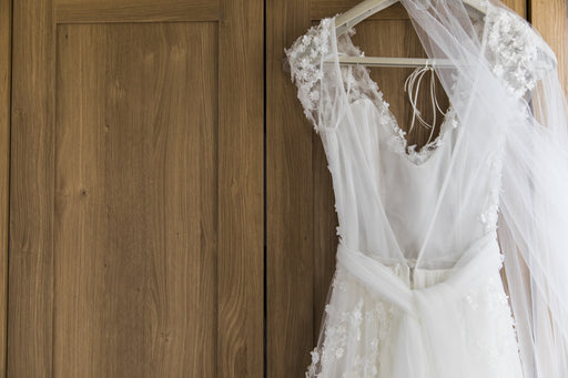 a pretty white wedding dress and veil hanging on a wooden door
