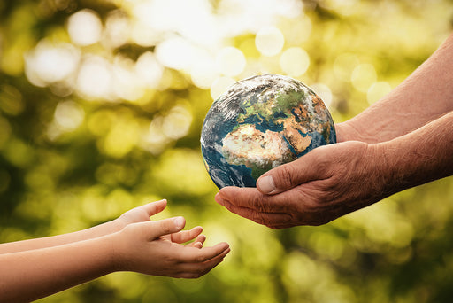 a pair of elderly hands passing a model of the earth to the hands of a child