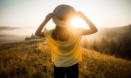 a woman looking over a sunset view of hills holding onto her straw boater