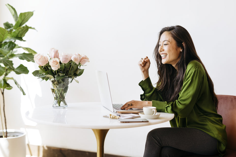 a woman in a green silk shirt working on her laptop